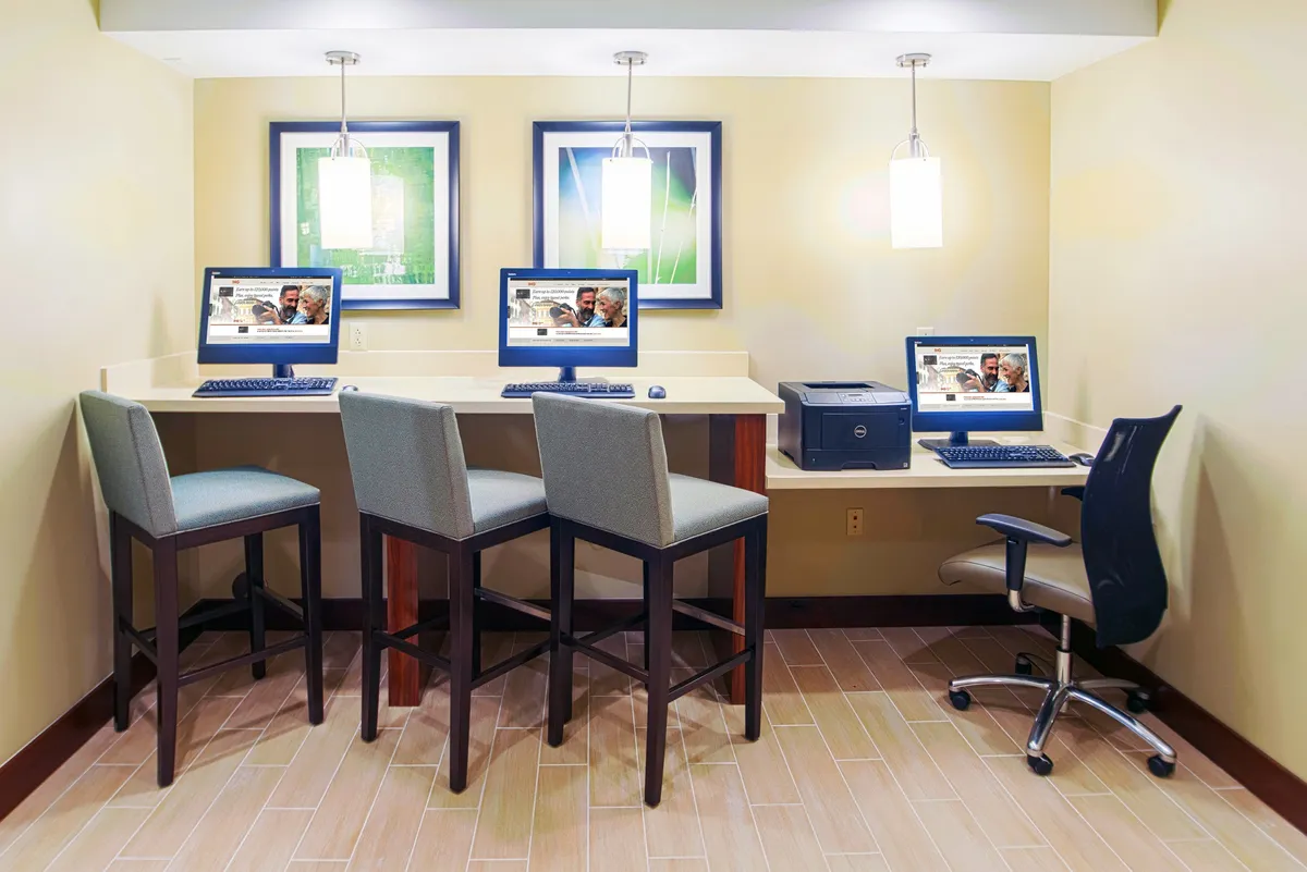 A modern business center with computers, stools, a printer, and vibrant artwork on the walls. The atmosphere is productive yet welcoming, ideal for business travelers needing to work or print essential documents.