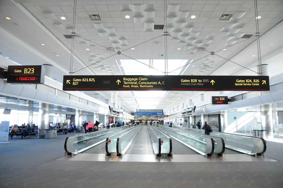 A bustling airport interior with moving walkways, information displays, comfortable seating areas, and travelers in motion. The scene conveys anticipation, movement, and the convenience of travel to and from Denver.