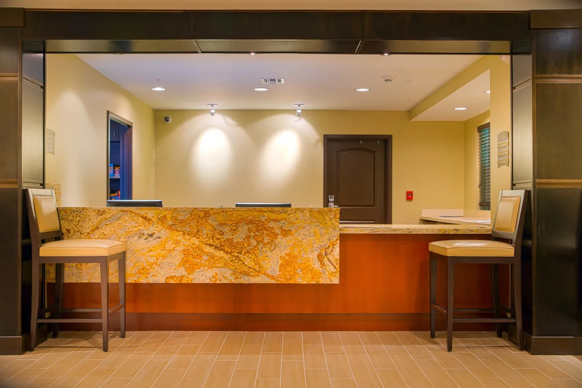 An inviting guest services area with a welcoming reception counter, comfortable seating stools, and tasteful wall decor. The space exudes hospitality and professionalism, providing a friendly first impression for all guests.