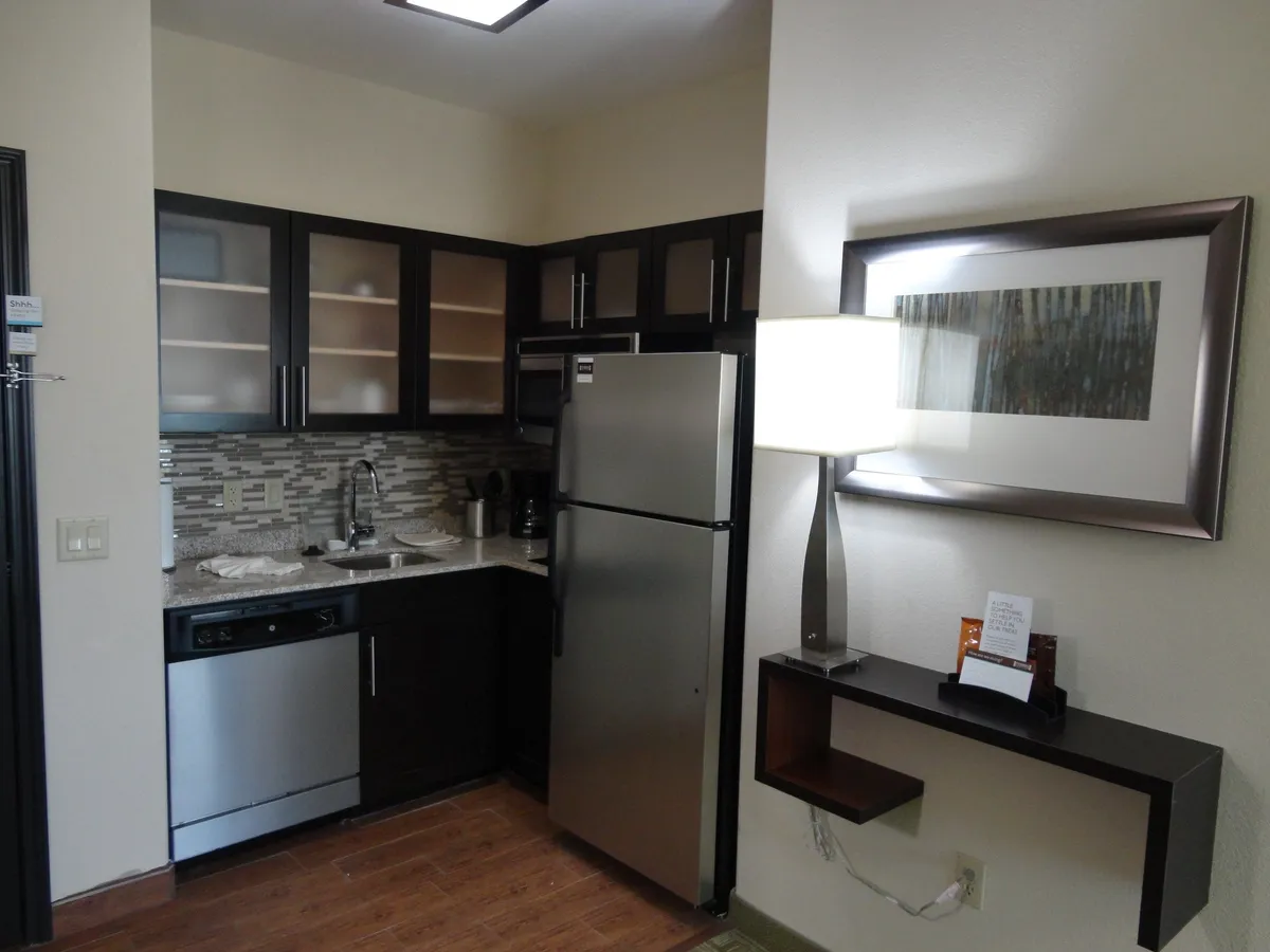 A contemporary kitchen scene featuring stainless steel appliances, a granite countertop, and stylish overhead lighting. The space is arranged for both cooking and entertaining, with clear access to the stove, microwave, refrigerator, and dishwasher. Artwork on the wall adds a personal touch, and the setting is warm and welcoming.