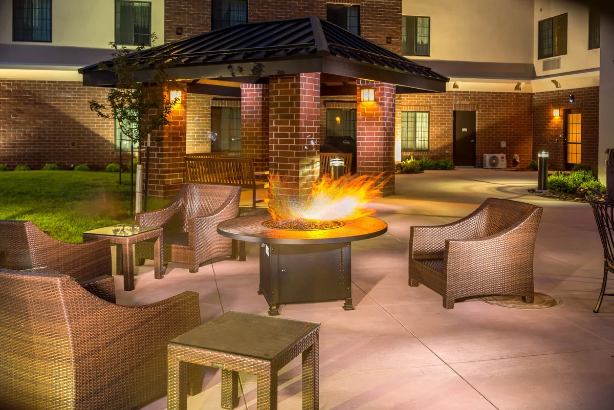 An inviting outdoor communal space featuring a fire pit surrounded by wicker chairs and a sturdy brick structure. The area is clearly set up for social gatherings, outdoor dining, and evening relaxation, making it a perfect spot for a classic cookout or BBQ with friends or family.