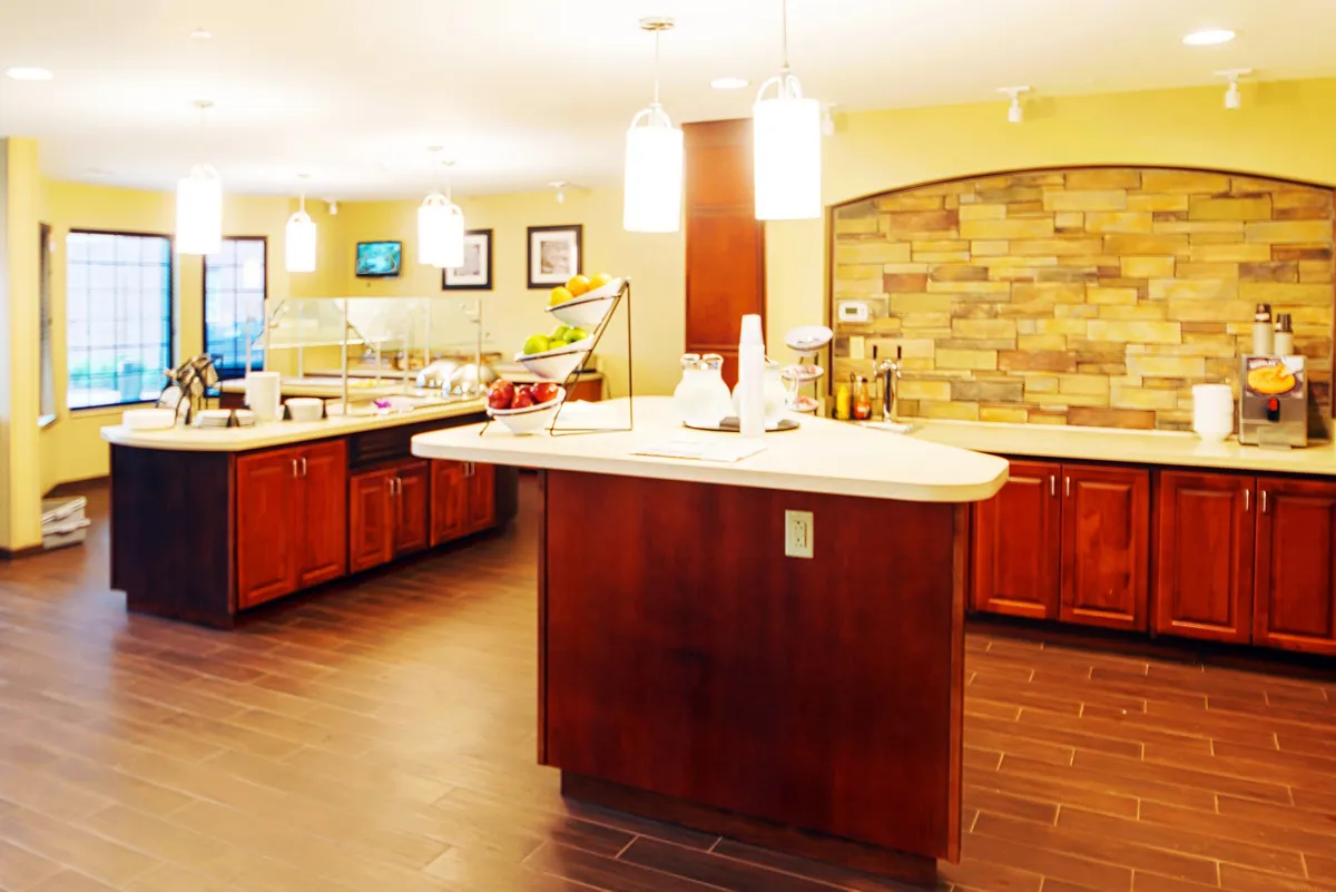 This image showcases an interior with a central island counter, stone accent wall, and hanging light fixtures. The scene is warm and inviting, suitable for casual meals, coffee chats, or informal meetings. The fruit display and overall layout further reinforce a homey atmosphere.